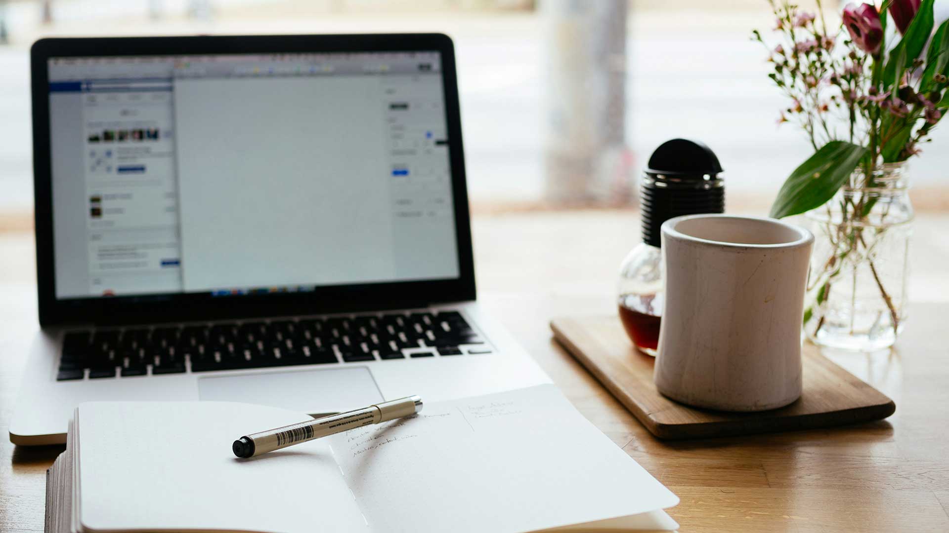 Ordinateur sur un bureau avec un cahier et un stylo devant et un café