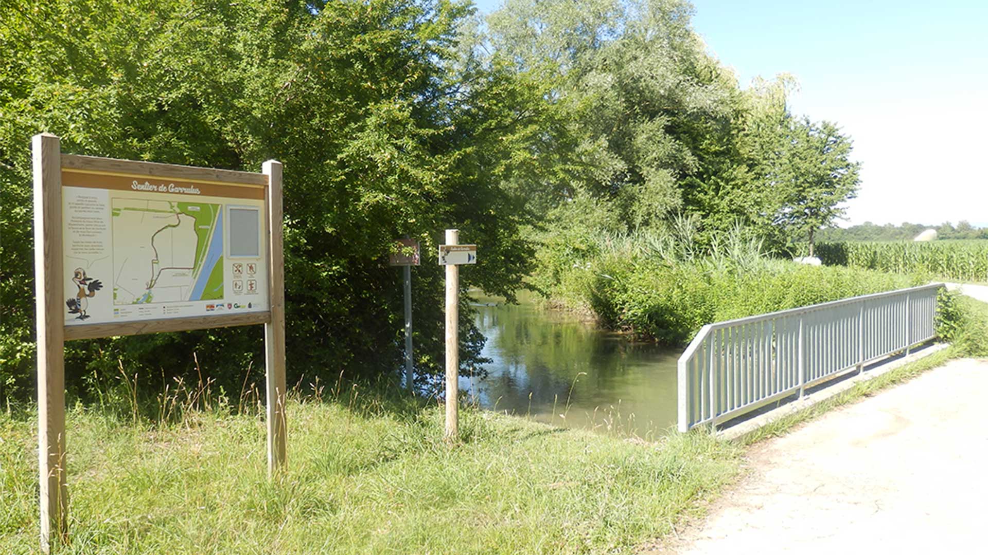 Sentier nature avec un pont avec rivière et un panneau