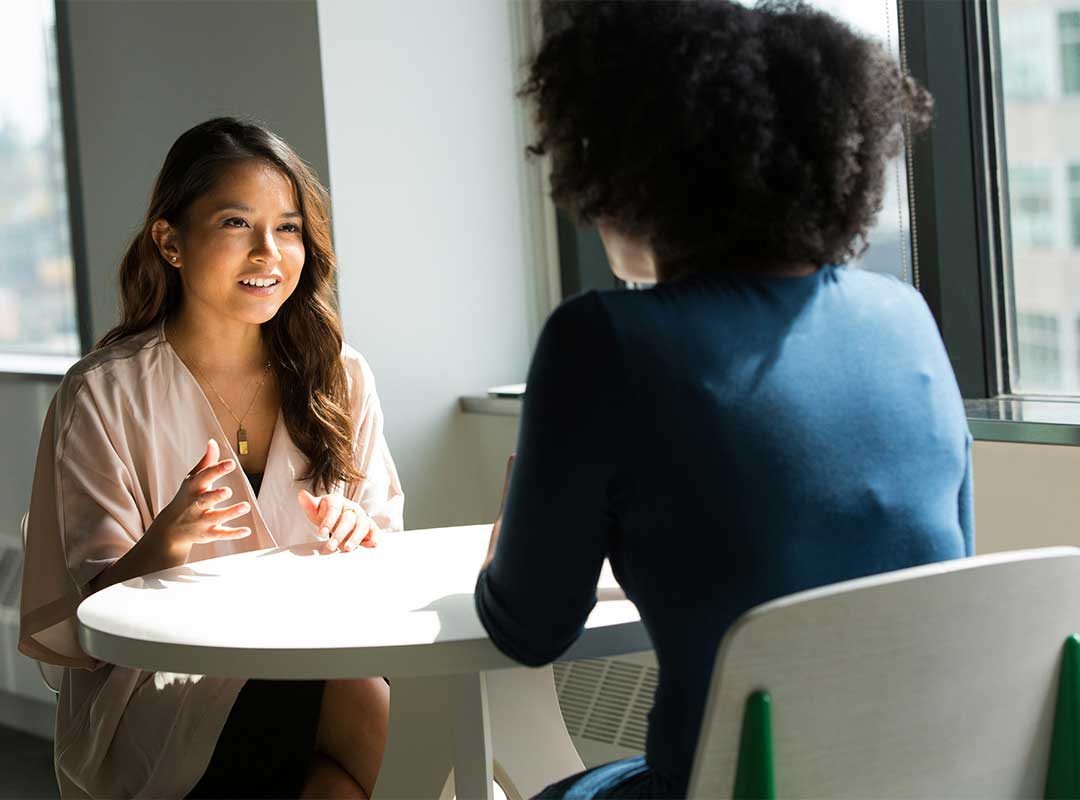 2 femme dont une de dos en entretient autour d'une table