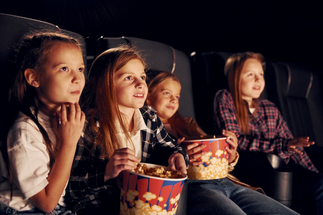 4 petites filles regardent un film au cinéma en mangeant des pop corn.